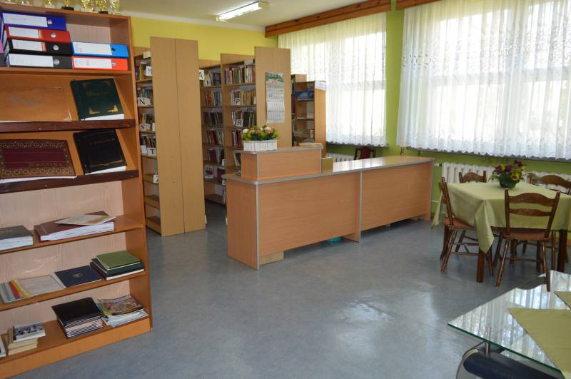 Biblioteka, w dalszej części trzy regały z książkami, z przodu stolik z krzesłami.